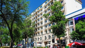 Un edificio de varios pisos con balcones, cielo azul despejado y árboles.