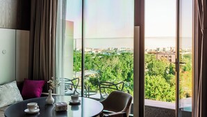 Una habitación moderna con una mesa redonda, sillas, un florero con flores y vistas a un paisaje urbano a través de grandes ventanales.