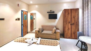 A hotel room with a bed, a sofa, a TV, a wooden wardrobe, and a ceiling fan. - Hotel H - 22 (Noida)