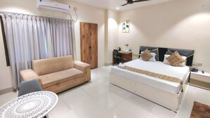 A hotel room with a bed, a sofa, a desk, a chair, a small table, an air conditioner, and a ceiling fan. - Hotel H - 22 (Noida)