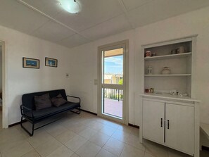 Ein Zimmer mit einer Couch, einer zur Außenseite führenden Tür und einem weißen Schrank mit Regalen.