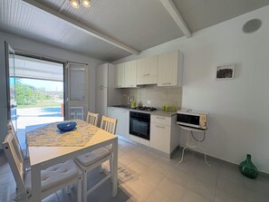 Ett kompakt kök med vita skåp, ett matbord med stolar, en inbyggd ugn och en mikrovågsugn.