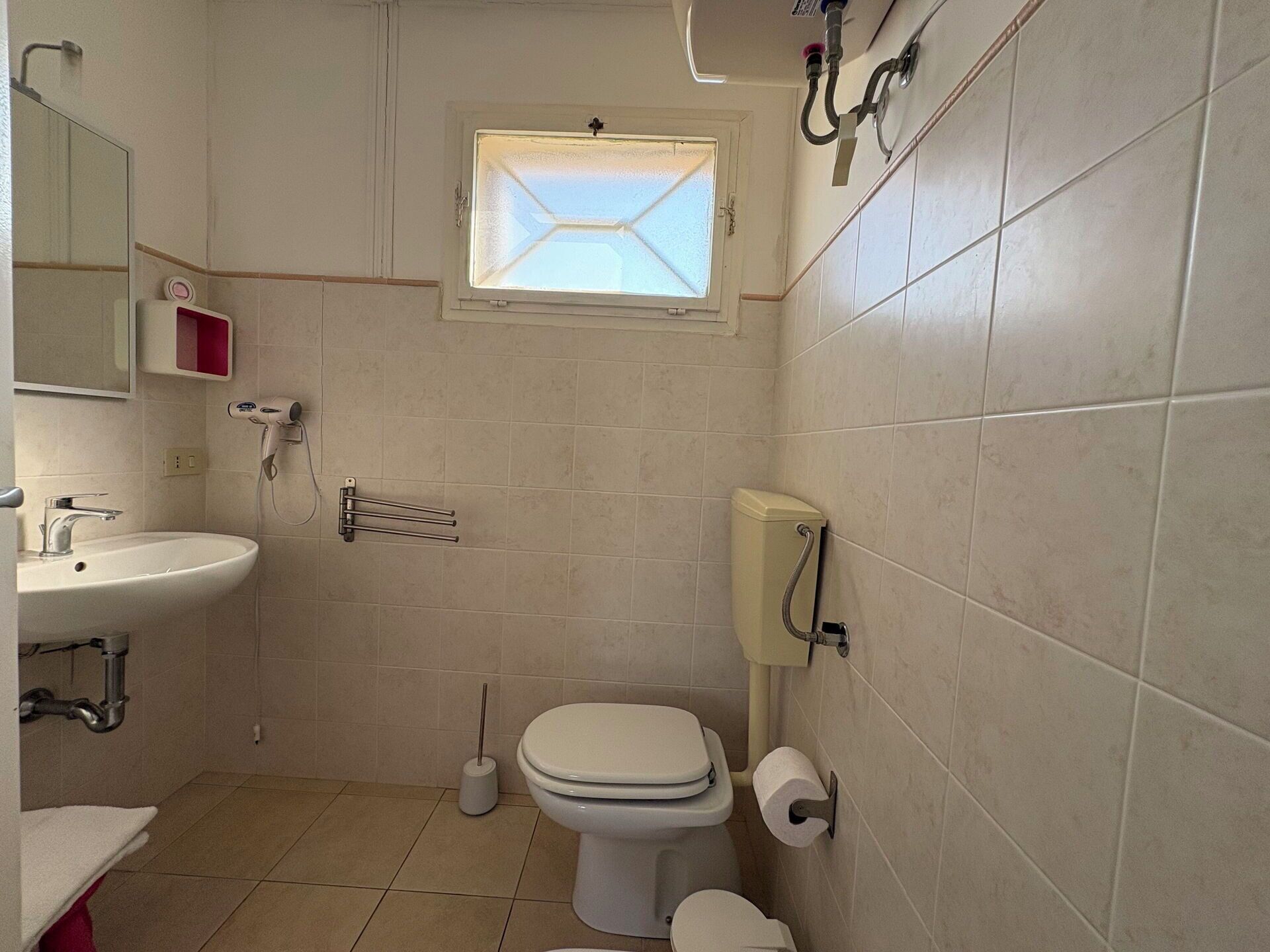 Et lille badeværelse med toilet, håndvask og et vindue.