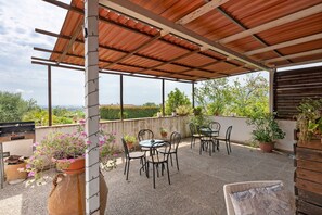An outdoor patio with tables and chairs, potted plants, and a view of the landscape.