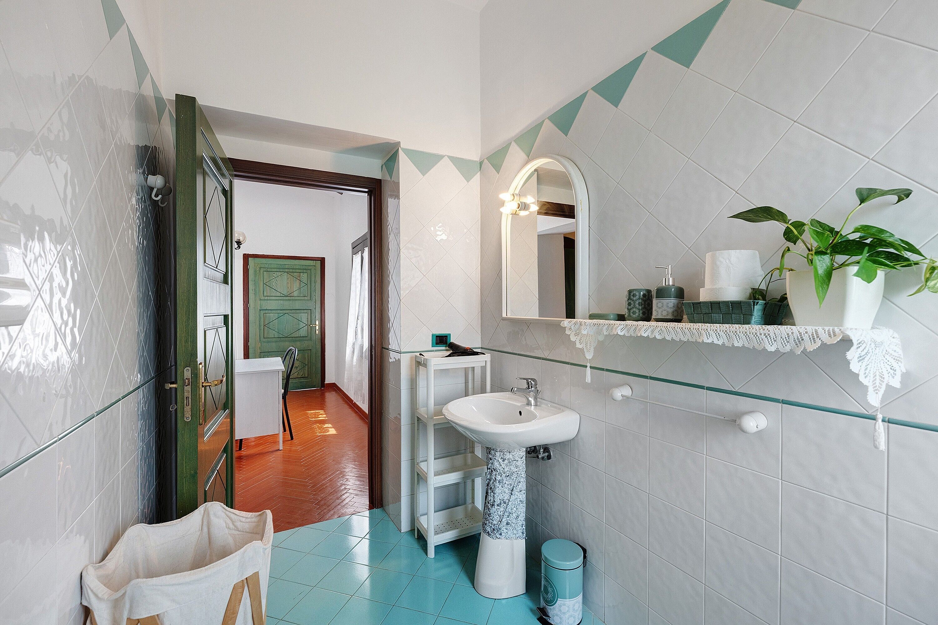 A bathroom with a white sink, a mirror, a green door, and a potted plant.