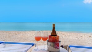 A beach scene with two glasses of pink drink, a bottle of champagne, and a bucket on a table. - West Bay Club first floor Coach Home with Lake View (Estero)