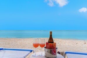 A beach scene with two glasses of pink drink, a bottle of champagne, and a bucket on a table. - West Bay Club first floor Coach Home with Lake View (Estero)