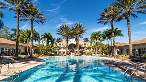 A resort with a central pool, palm trees, and a building with a tiled roof. - West Bay Club first floor Coach Home with Lake View (Estero)