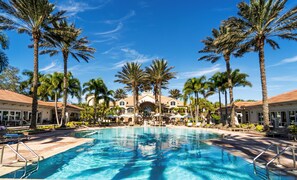A resort with a central pool, palm trees, and a building with a tiled roof. - West Bay Club first floor Coach Home with Lake View (Estero)