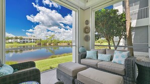 A covered patio with wicker furniture, a view of a lake, and a building in the background. - West Bay Club first floor Coach Home with Lake View (Estero)