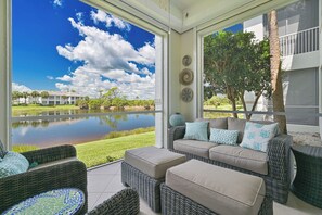 A covered patio with wicker furniture, a view of a lake, and a building in the background. - West Bay Club first floor Coach Home with Lake View (Estero)