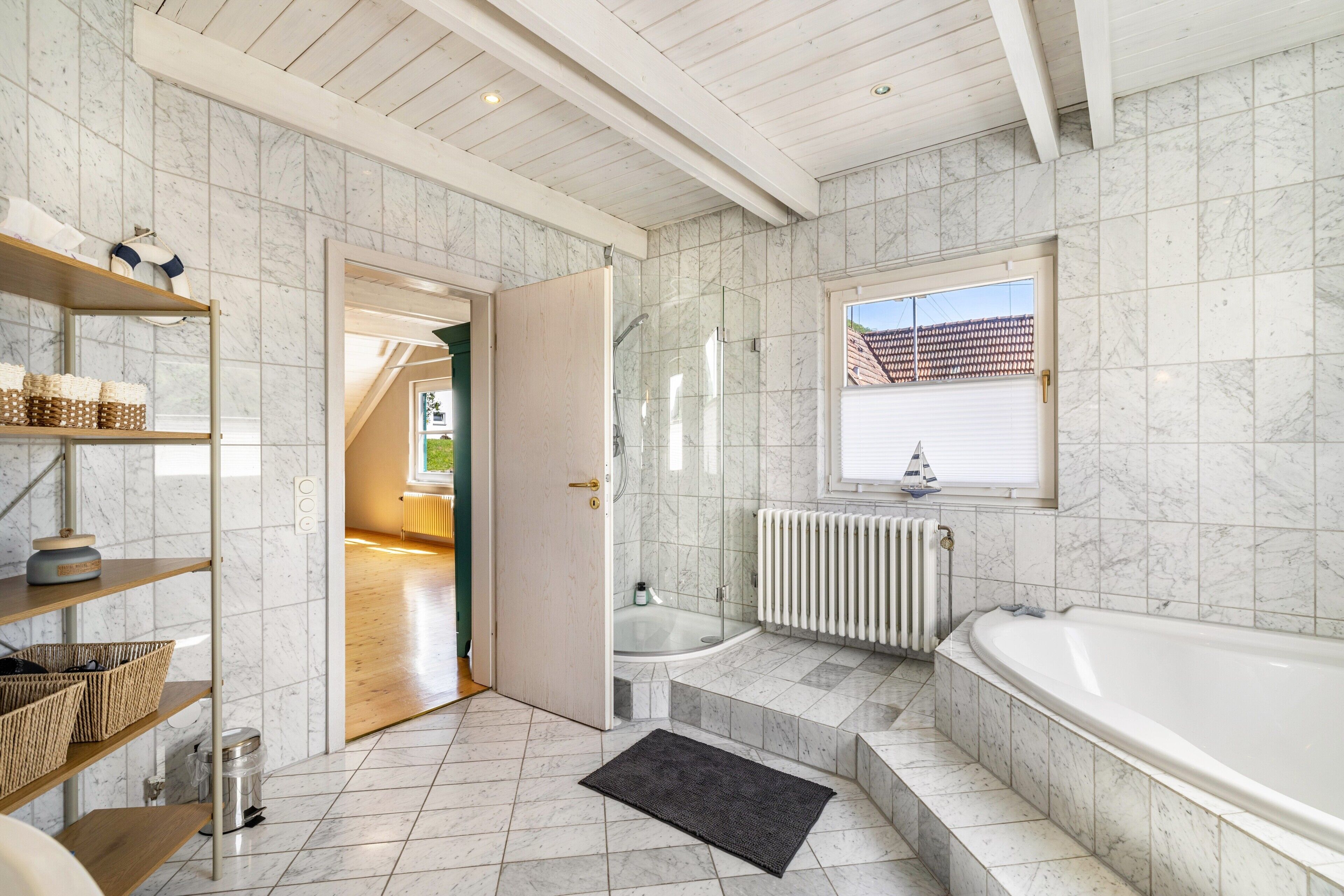 Une salle de bain avec une baignoire, une douche, une fenêtre donnant sur un paysage agréable et une porte menant à une autre pièce.