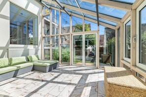 A sunlit room with a glass ceiling, a sofa, a wicker table, and a view of the outside.