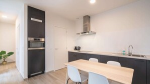 A modern kitchen with a built-in oven, a stainless steel range hood, and a wooden dining table with chairs. - City Rhythm Abode for 10 in Antwerp (Antwerp)