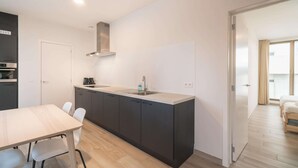 A modern kitchen with a central island, a dining table with chairs, and a view into a bedroom with a bed and window. - City Rhythm Abode for 10 in Antwerp (Antwerp)