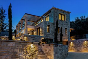 A modern stone house with a balcony, stone walls, and outdoor lighting. - BRAND NEW LUXURY 4-BEDROOM VILLA IN CENTRAL LOCATION -70 METERS FROM THE SEA! (Nydri)