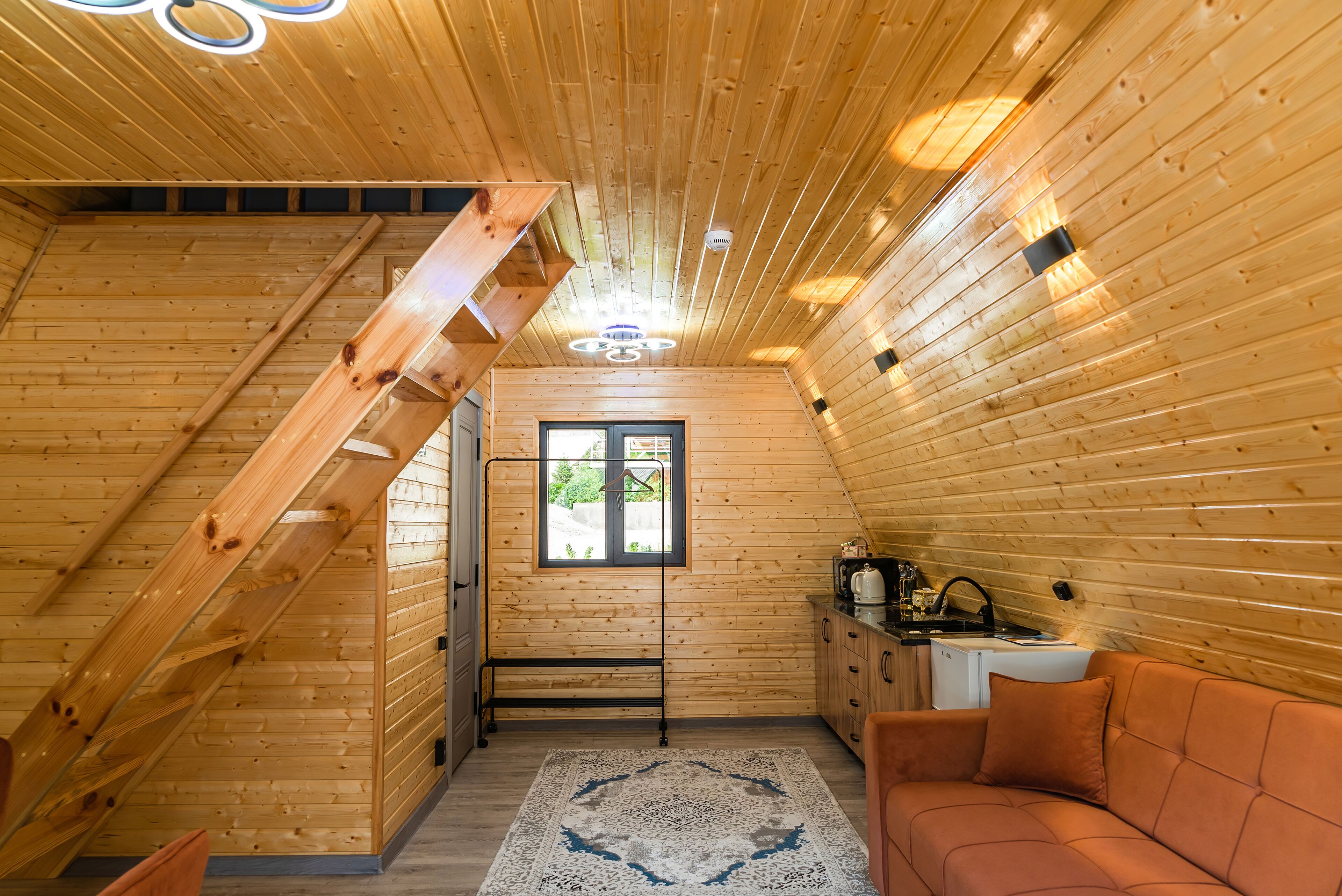 A wooden cabin interior with a loft bedroom, a kitchen area, and a seating area.