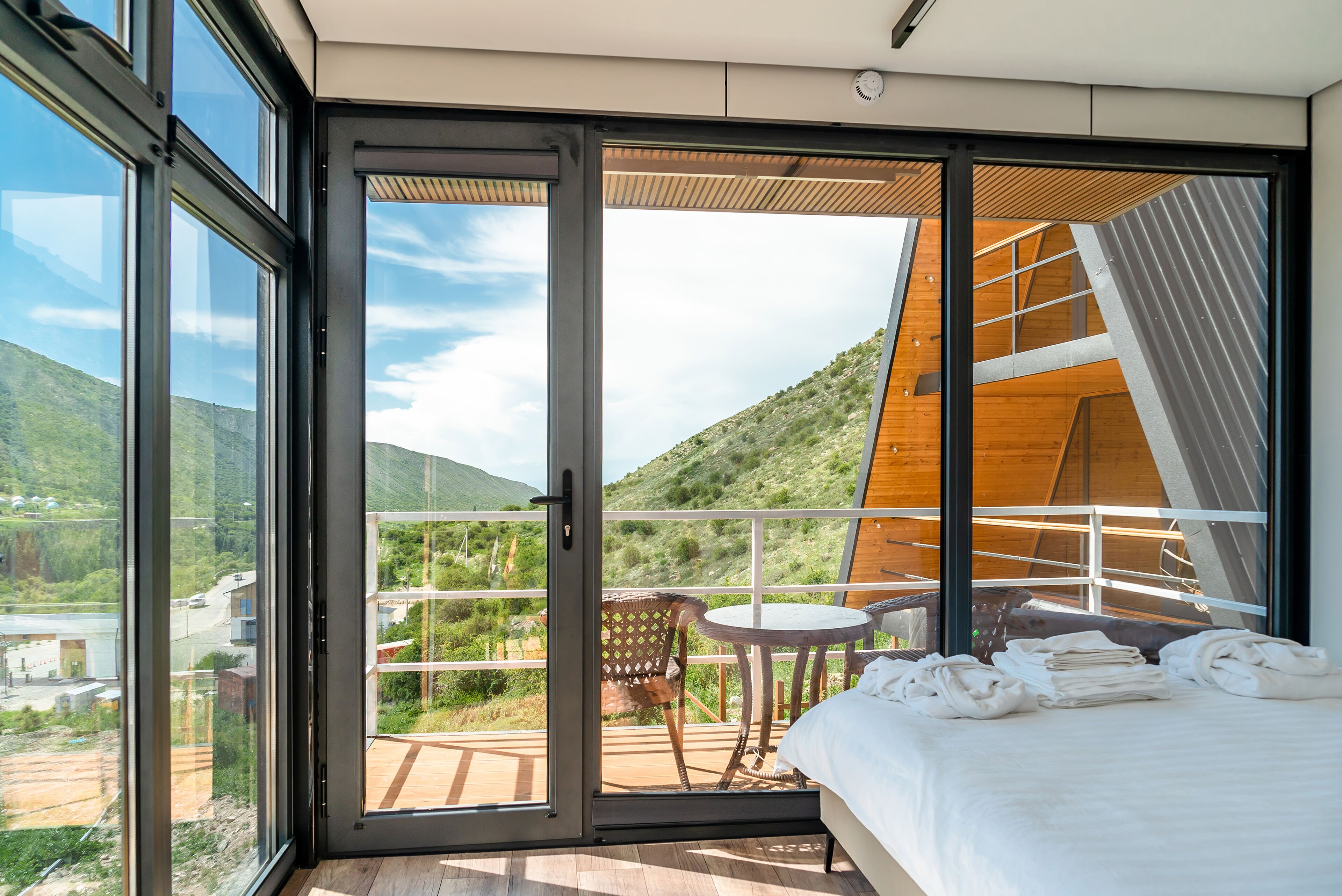 A modern bedroom with a large sliding glass door leading to a balcony with a view of a mountainous landscape.