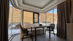 Una habitación moderna con sofá, dos sillones, una mesa y ventanas amplias que ofrecen vistas a un paisaje nevado.