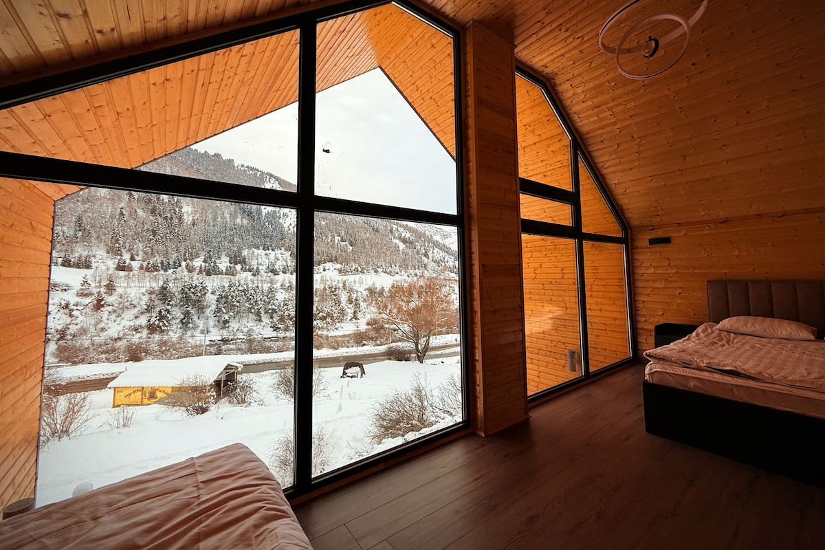 A room with large windows, a bed, and a wooden ceiling.