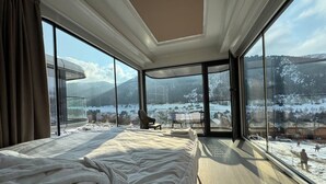 Un dormitorio con una cama grande, una silla y vistas a un paisaje nevado a través de amplios ventanales.