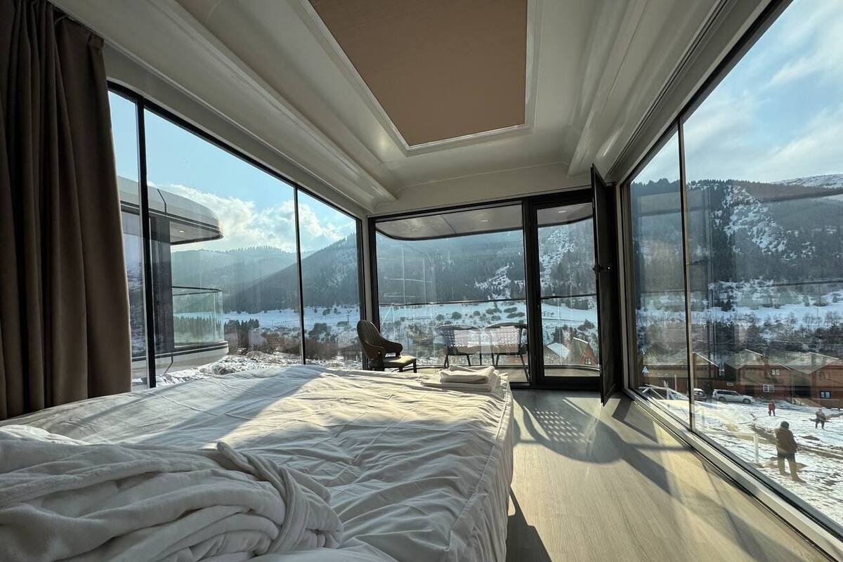 A bedroom with a large bed, a chair, and a view of a snowy landscape through large windows.