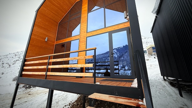 Una cabaña de madera con balcón, ventanas amplias y vistas a un paisaje nevado.