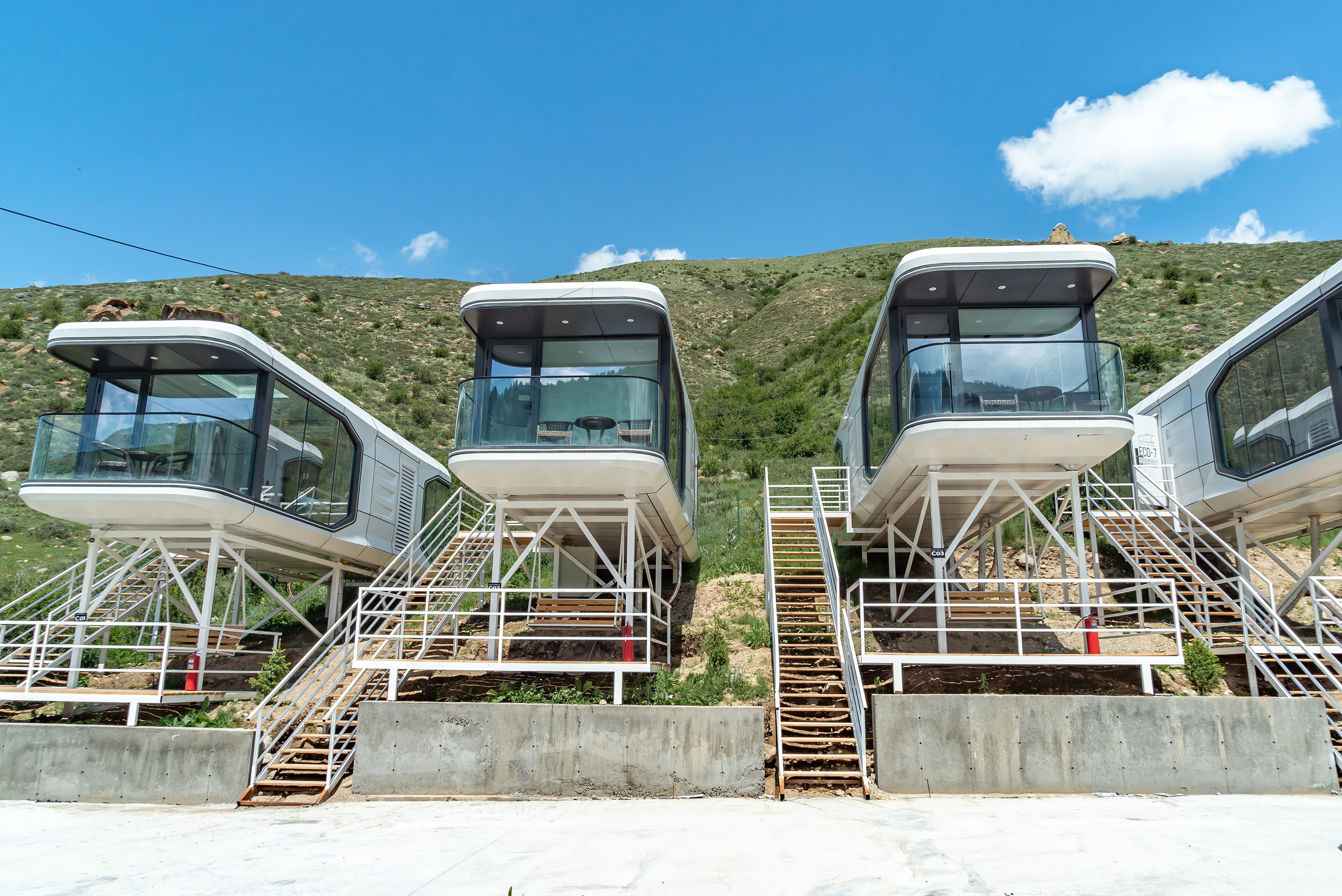 Three cable car cabins with glass walls, metal stairs, and a mountainous backdrop.