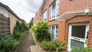 A narrow brick pathway flanked by residential buildings with visible windows and a wooden fence on one side. - Grambker Heerstraße (Bremen)