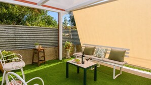 Une terrasse avec un banc blanc, une table et un pot de fleurs.