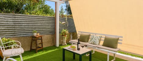 A patio with a white bench, a table, and a potted plant.