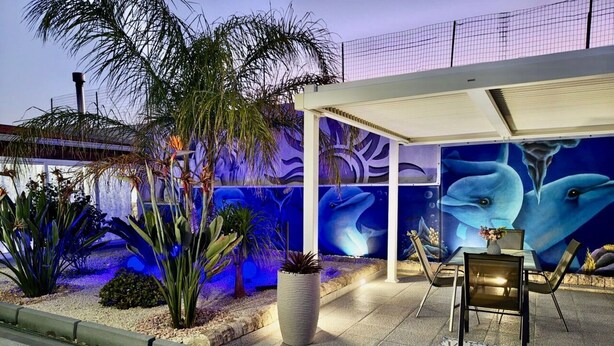 A covered outdoor seating area with a mural of dolphins, a palm tree, and a potted plant. - Wonderful  villa with A/C, private pool, WIFI, TV, patio, pets allowed and panoramic view (Marina Di Ragusa)