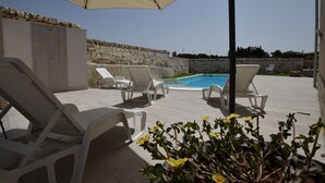 A poolside area with lounge chairs, a stone wall, and a clear sky. - Wonderful  villa with A/C, private pool, WIFI, TV, patio, pets allowed and panoramic view (Marina Di Ragusa)