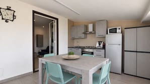 A compact kitchen with grey cabinets, a microwave, a refrigerator, and a dining area with a table and chairs. - Stunning  villa for 4 guests with A/C, WIFI, private pool, TV, patio and panoramic view (Marina Di Ragusa)