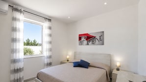 A bedroom with a bed, a nightstand, a lamp, and a window with curtains. - Stunning  villa for 4 guests with A/C, WIFI, private pool, TV, patio and panoramic view (Marina Di Ragusa)