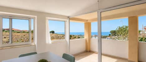 A modern interior with a dining area, large windows, and a view of the sea.