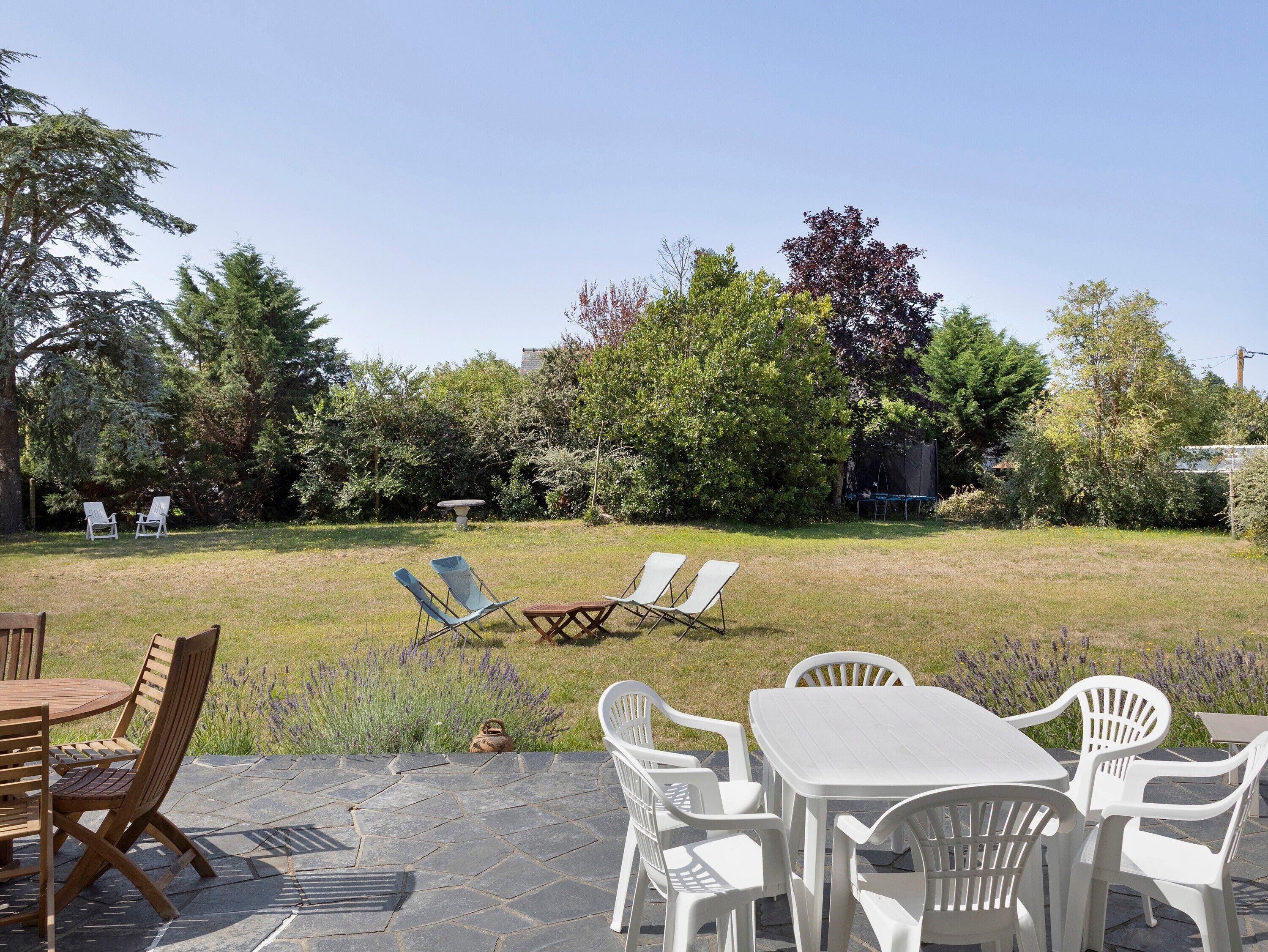 Eine Terrasse mit Tisch und Stühlen, ein grüner Rasen und Bäume im Hintergrund.