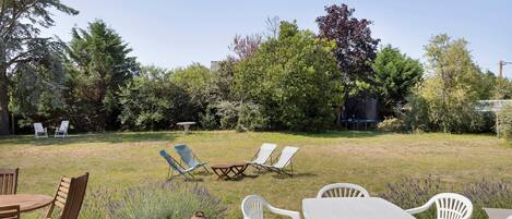 A patio area with a table and chairs, a grassy lawn, and trees in the background.
