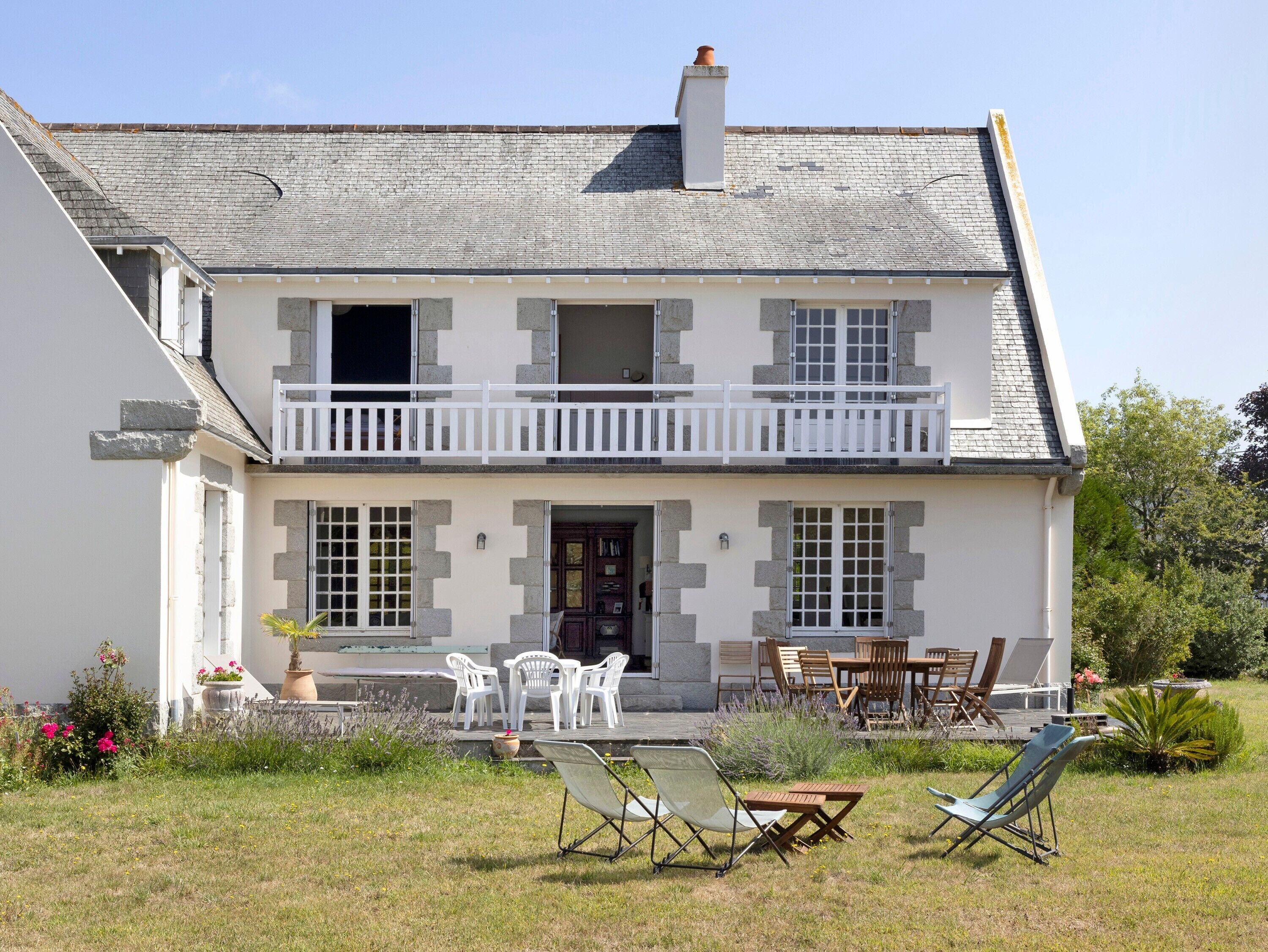 A two-story house with a balcony, a front porch with outdoor furniture, and a garden area.
