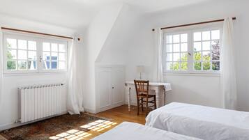 Une chambre avec deux lits, un bureau avec une chaise, un radiateur et une fenêtre avec des rideaux.