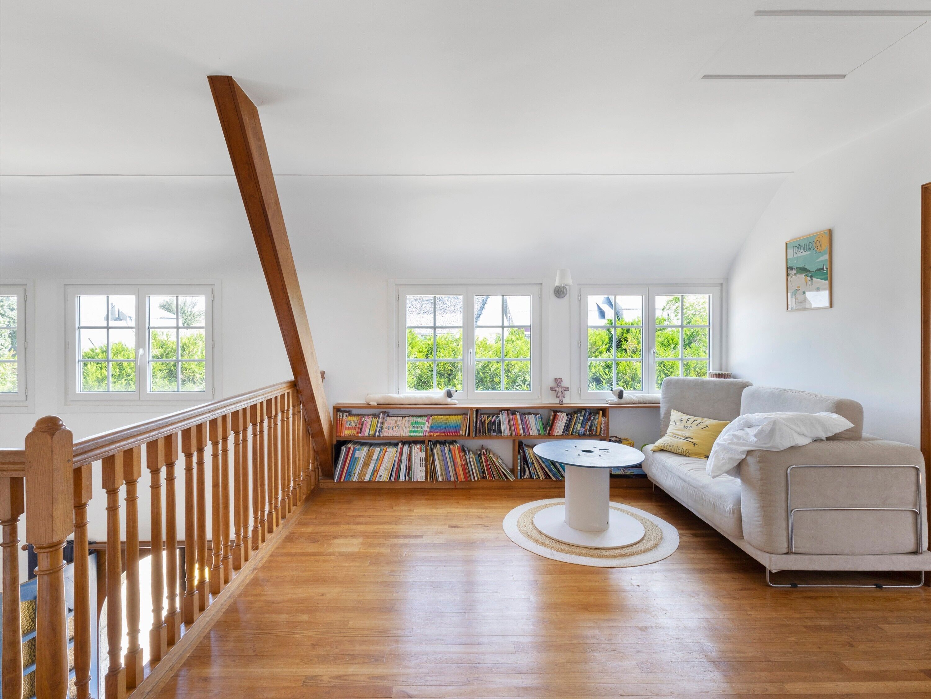 Ein geräumiges Zimmer mit einer Holztreppe, einer Sitzecke mit Sofa und rundem Tisch sowie einem Bücherregal voller Bücher.