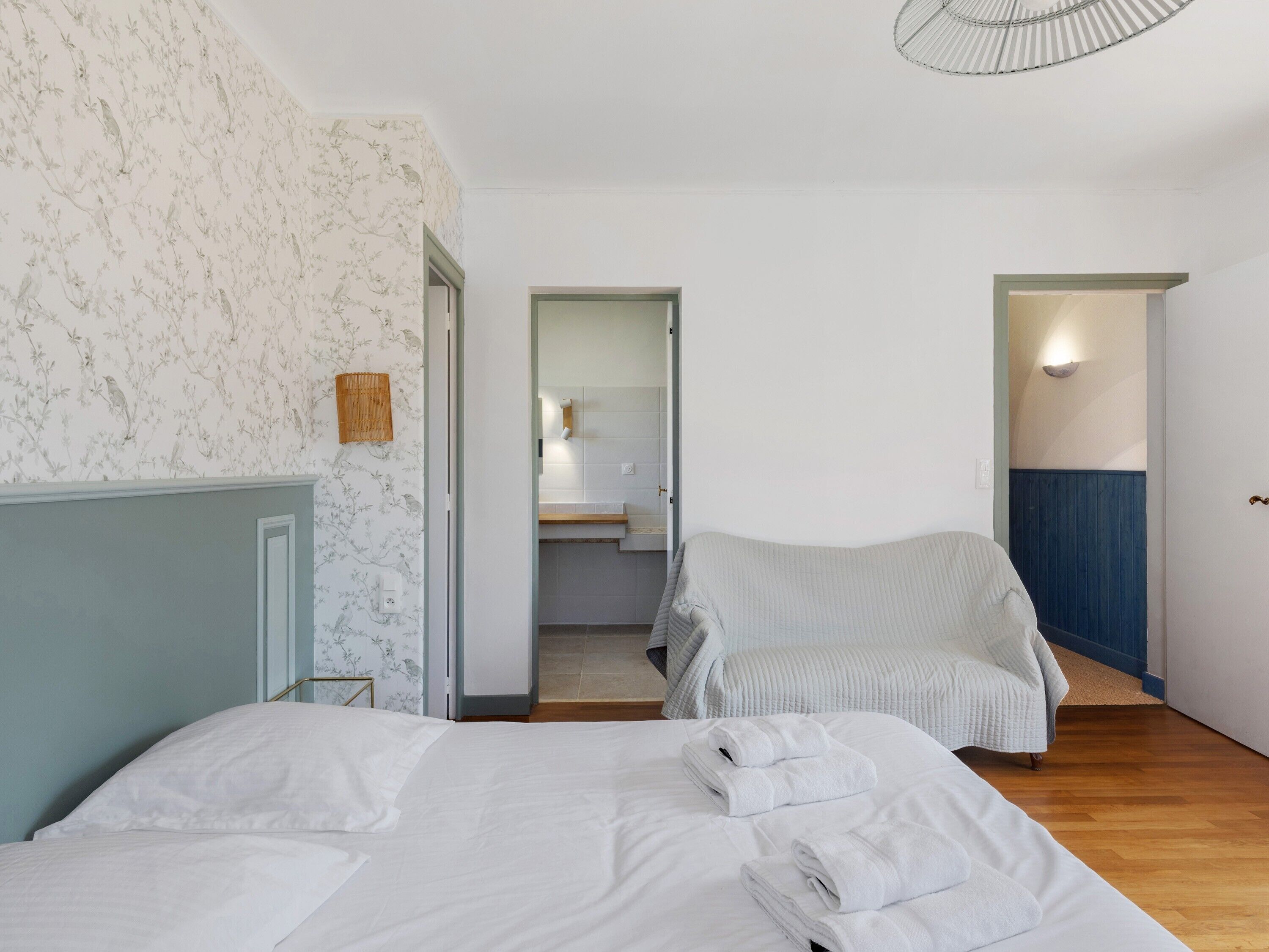 Une chambre avec deux lits, une salle de bain visible à travers une porte ouverte et une chaise.