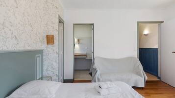 Une chambre avec deux lits, une salle de bain visible à travers une porte ouverte et une chaise.