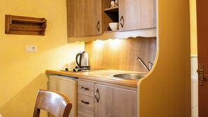Une cuisine avec des meubles de rangement en bois, un évier, une bouilloire et une chaise.