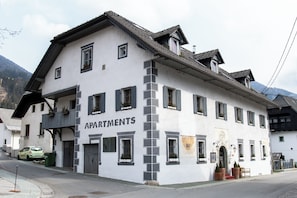 A white building with 'APARTMENTS' signage, multiple windows, balconies, and a mountain backdrop. - Apartments Belopeški Dvori (Kranjska Gora)