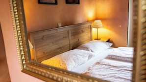 Un lit avec une tête de lit en bois, une lampe de chevet et un miroir qui reflète la pièce.