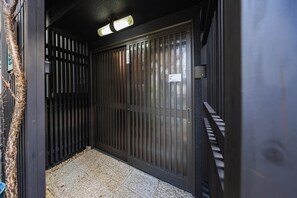 A narrow hallway with a metal gate, a textured mat at the entrance, and a ceiling light fixture. - Deer Path Nara (Narashi Takamikadocho)