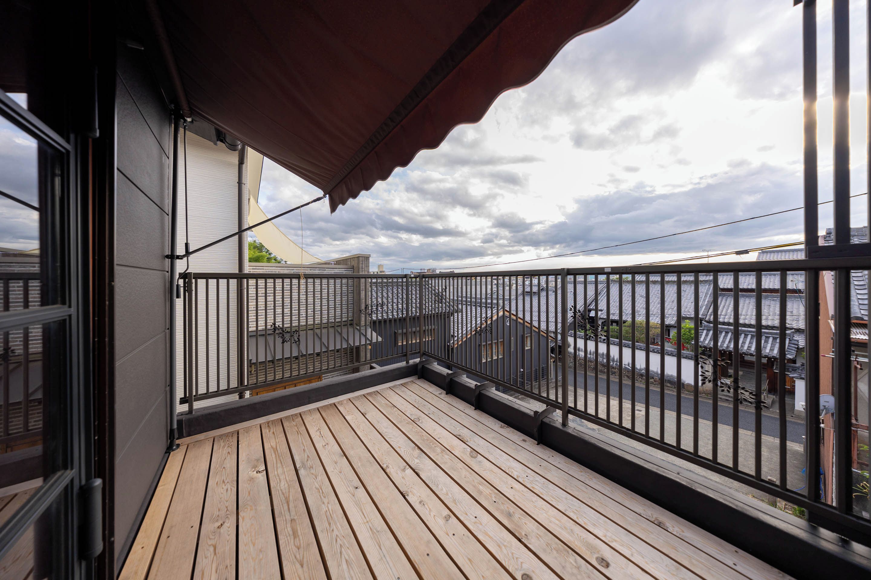 Una terraza de madera con barandilla metálica, un toldo rojo y vistas a edificios y una masa de agua.