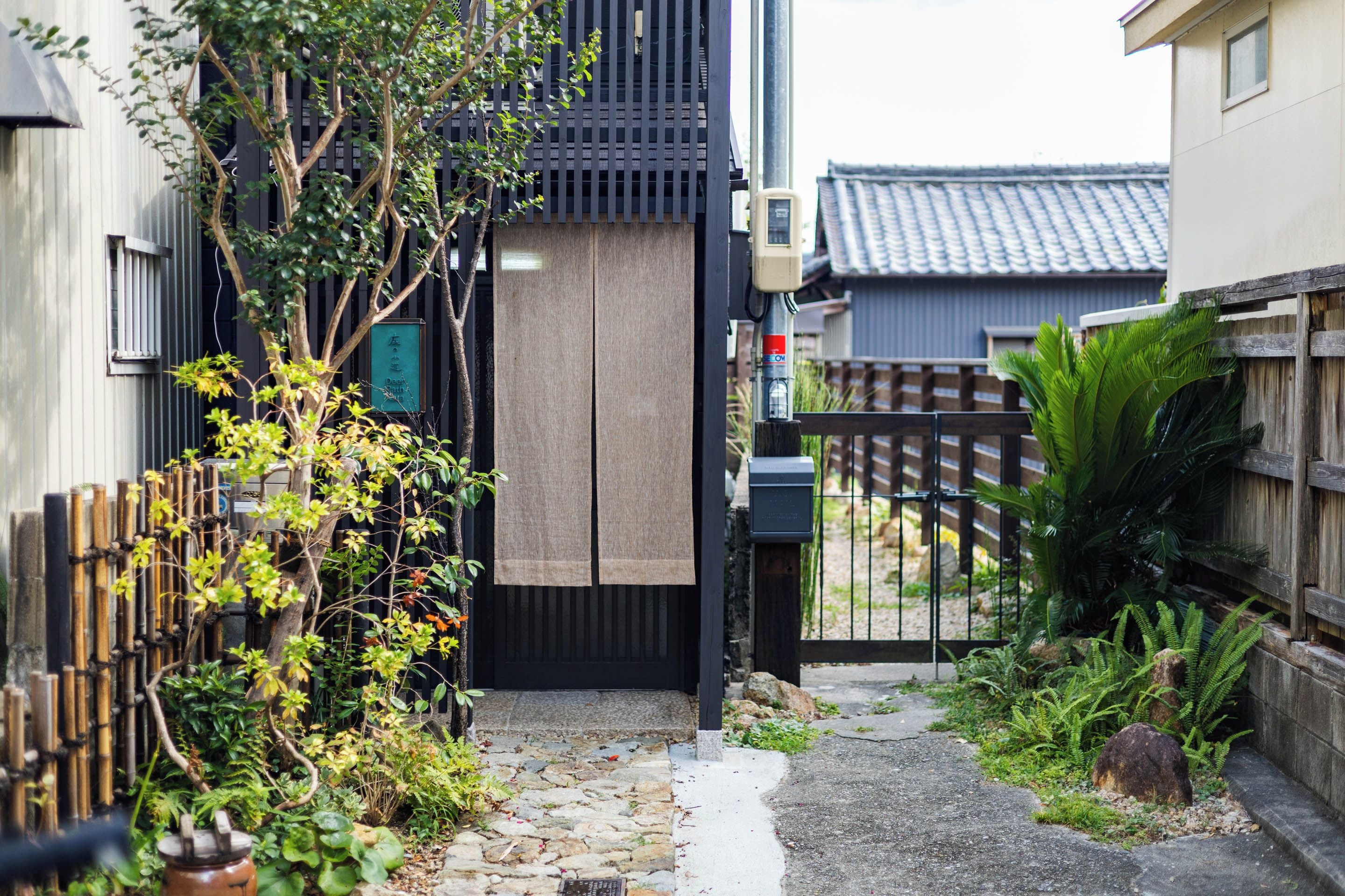 A narrow alleyway with a wooden fence on one side and a building with a black gate on the other.