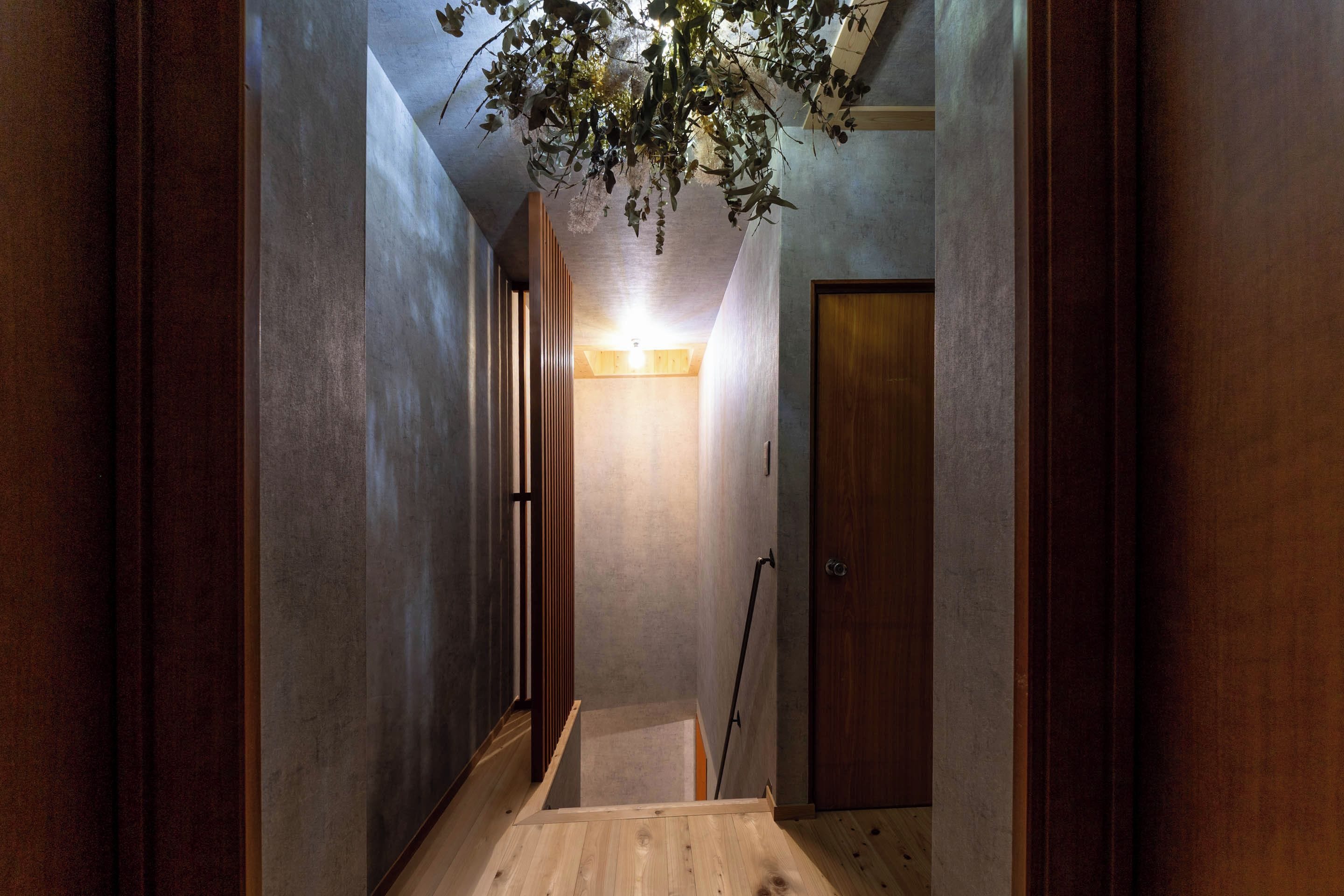 Un pasillo estrecho con suelo de madera, una puerta al final y una planta colgante.